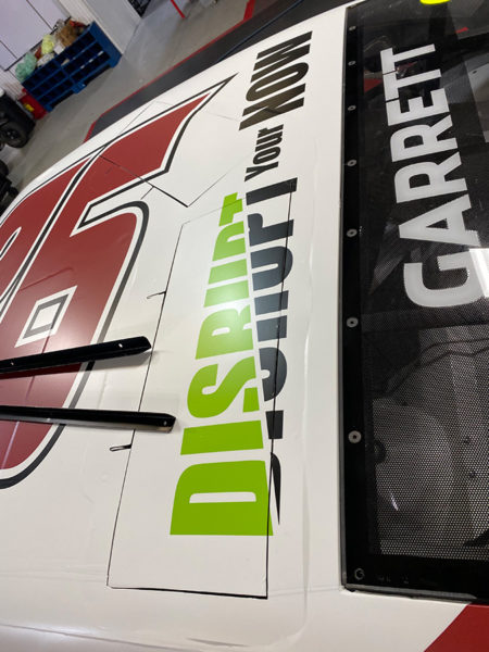 photo of top of Colin Garrett's race car, showing the Disrupt Your Now logo